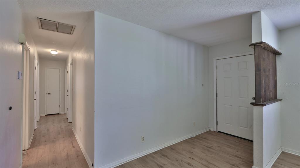 A hallway with light wood-look flooring leads to closed doors, adjacent to an entryway area — 2508 PINE TREE DRIVE, EDGEWATER, FL