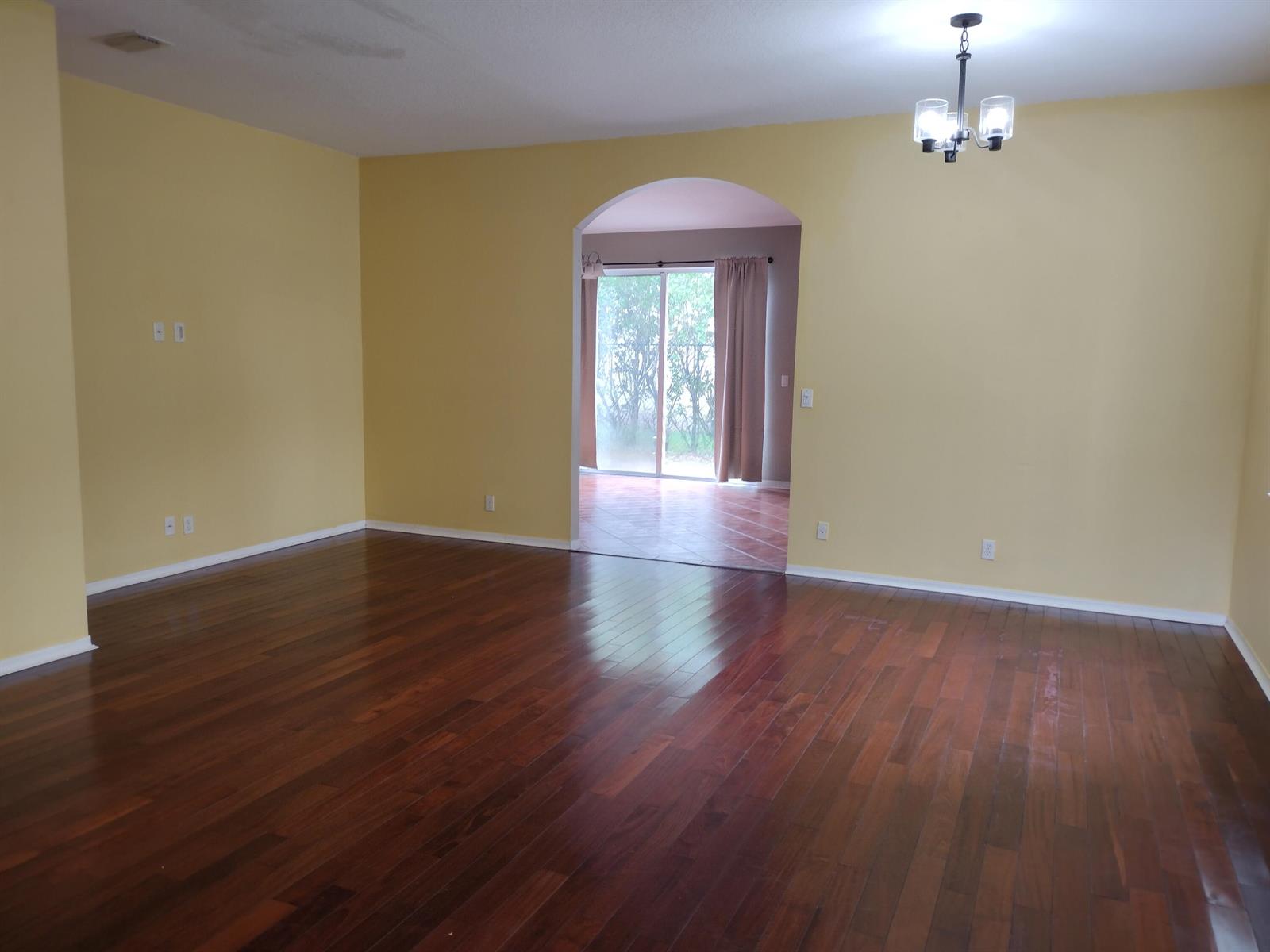 An empty room with yellow walls, dark wood flooring, and an arched doorway to a patio — 1738 Pierside Circle, Wellington FL 33414, WELLINGTON, FL