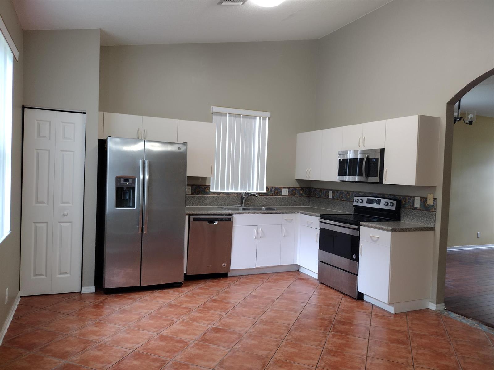 A kitchen features white cabinets, stainless steel appliances, granite countertops, and terracotta tile flooring — 1738 Pierside Circle, Wellington FL 33414, WELLINGTON, FL