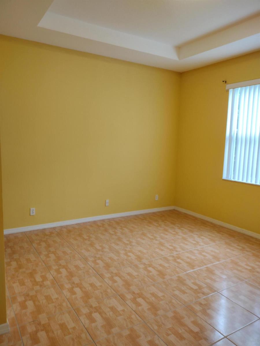 An empty room with yellow walls, tile flooring, and a tray ceiling with a window — 1738 Pierside Circle, Wellington FL 33414, WELLINGTON, FL