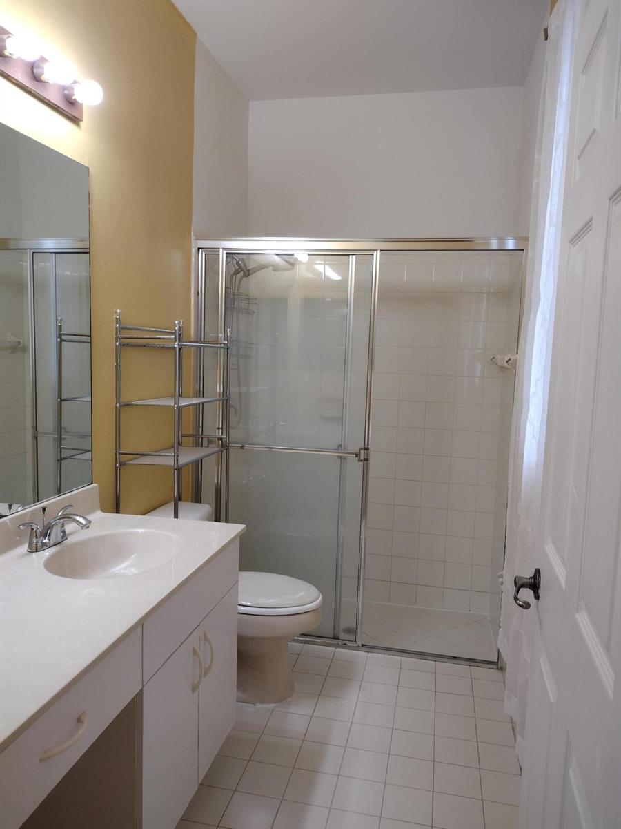 A bathroom features a white vanity, a toilet, and a glass-enclosed shower with white tiles — 1738 Pierside Circle, Wellington FL 33414, WELLINGTON, FL