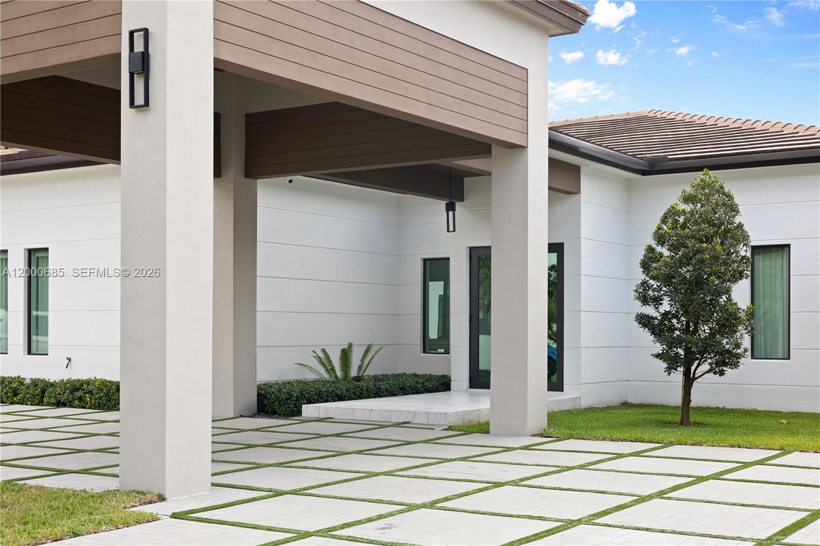 A modern white house exterior features a covered entryway with a grid-patterned paver driveway — 80 NW 129th Ave, Miami FL 33182, MIAMI, FL