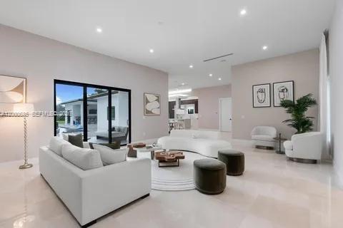 A bright, open-concept living room features white sofas, dark ottomans, and large sliding glass doors — 80 NW 129th Ave, Miami FL 33182, MIAMI, FL