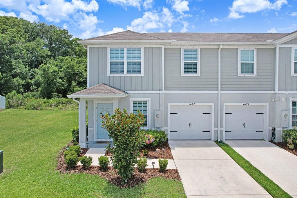 A two-story townhouse with light gray siding, a single-car garage, and a front entryway — 12214 GRIZZLY LANE, NEW PORT RICHEY, FL