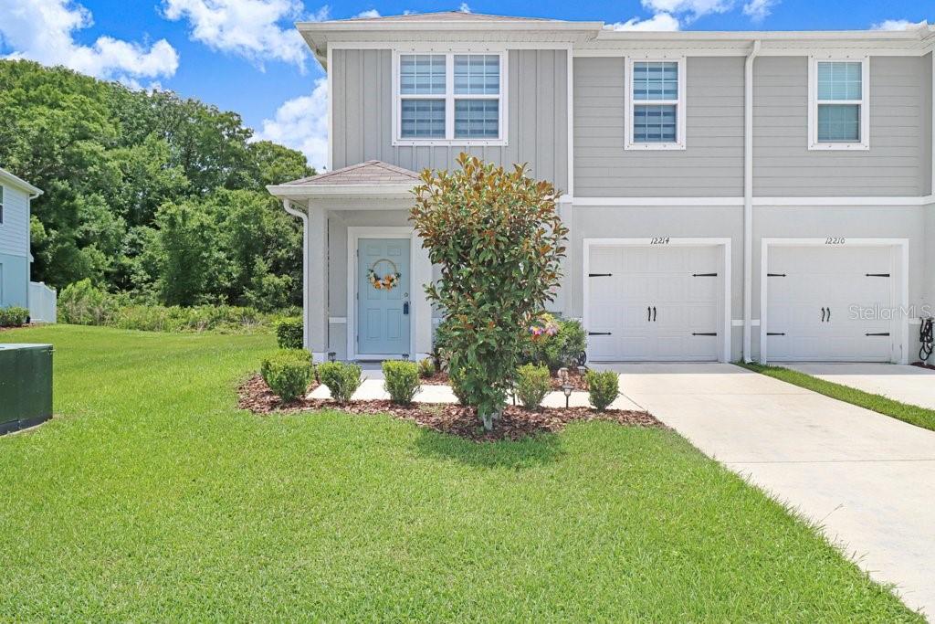 A two-story townhouse with a light blue front door, gray siding, and a concrete driveway — 12214 GRIZZLY LANE, NEW PORT RICHEY, FL