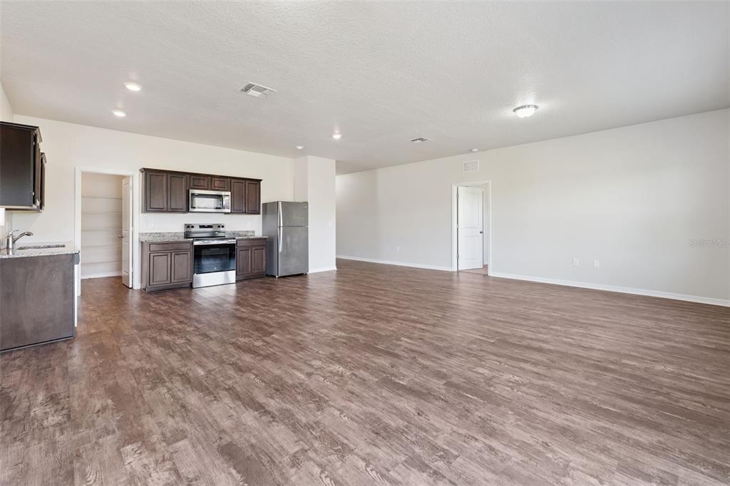 An open-concept kitchen with dark cabinets and stainless steel appliances overlooks a large living area — 409 STILLWATER LANE, HAINES CITY, FL