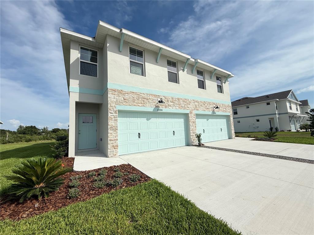 A two-story duplex with light-colored stucco, stone veneer, and two light blue garage doors — 13998 EMERALD FIELDS DRIVE Lot 23, HUDSON, FL