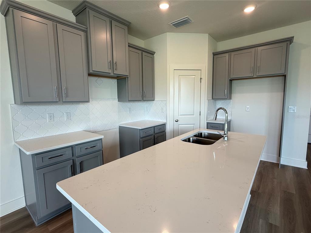 A kitchen features gray cabinets, white countertops, a center island, and a white tile backsplash — 13998 EMERALD FIELDS DRIVE Lot 23, HUDSON, FL