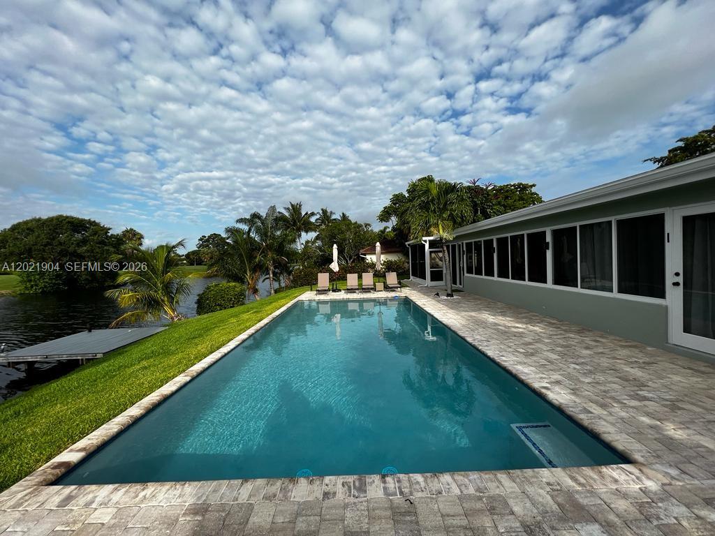 A rectangular swimming pool sits on a stone patio beside a house overlooking a lake — 3324 Lakeview Blvd, Delray Beach FL 33445, DELRAY BEACH, FL