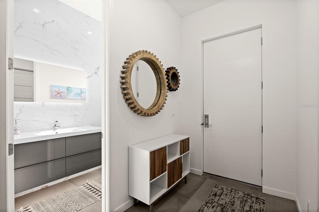 A modern entryway features a white cabinet, gear-shaped wall decor, and a view into a bathroom — 5351 MOELLER AVENUE, SARASOTA, FL