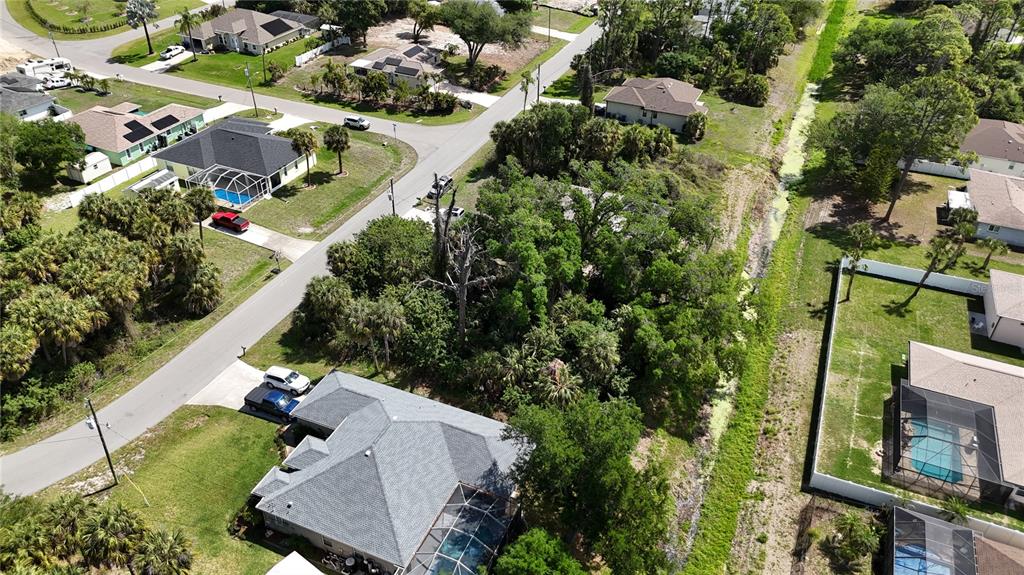 An aerial view shows a suburban neighborhood with houses, a wooded lot, and a canal — TUCSON ROAD, NORTH PORT, FL