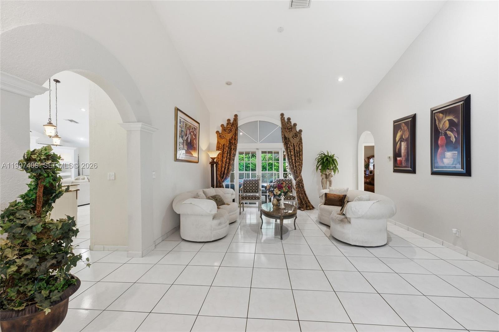 A bright living room features white tile floors, arched entryways, and two curved white sofas — 11400 NW 20th Ct, Plantation FL 33323, PLANTATION, FL