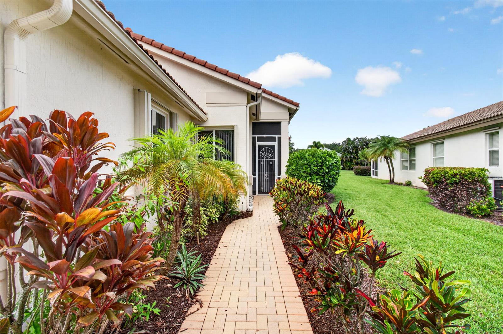 A paved walkway leads to a screened entryway beside a house with tropical landscaping — 2752 Clipper Circle, West Palm Beach FL 33411, WEST PALM BEACH, FL