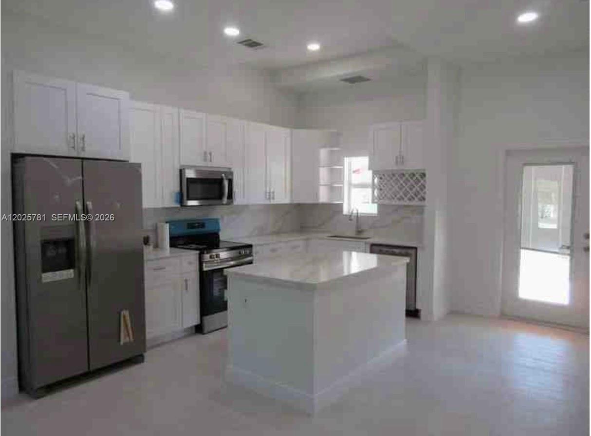 A modern kitchen features white cabinets, stainless steel appliances, and a central marble-topped island — LOXAHATCHEE, FL