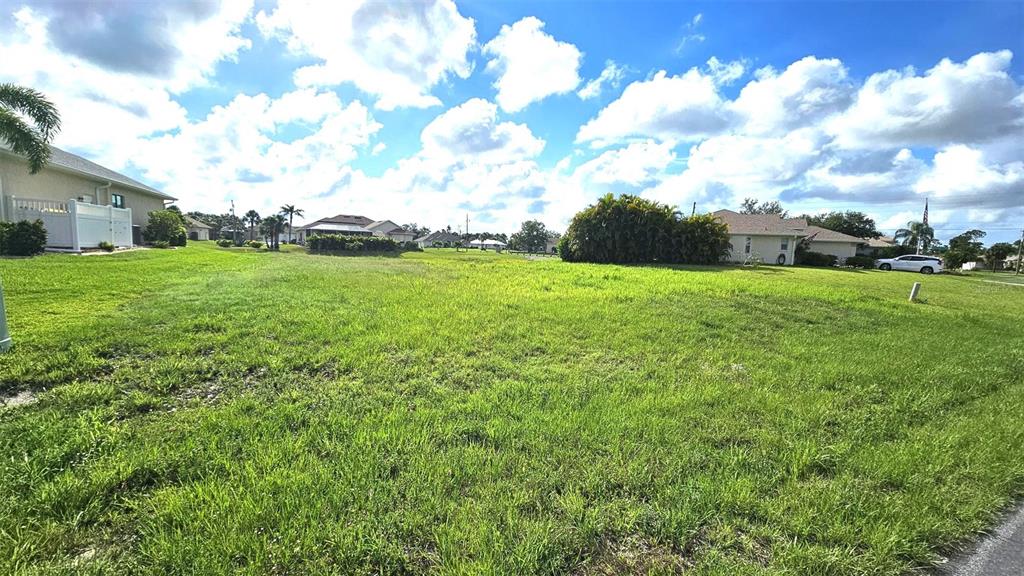 A grassy, vacant residential lot sits under a bright blue sky with scattered clouds — 144 LONG MEADOW LANE, ROTONDA WEST, FL