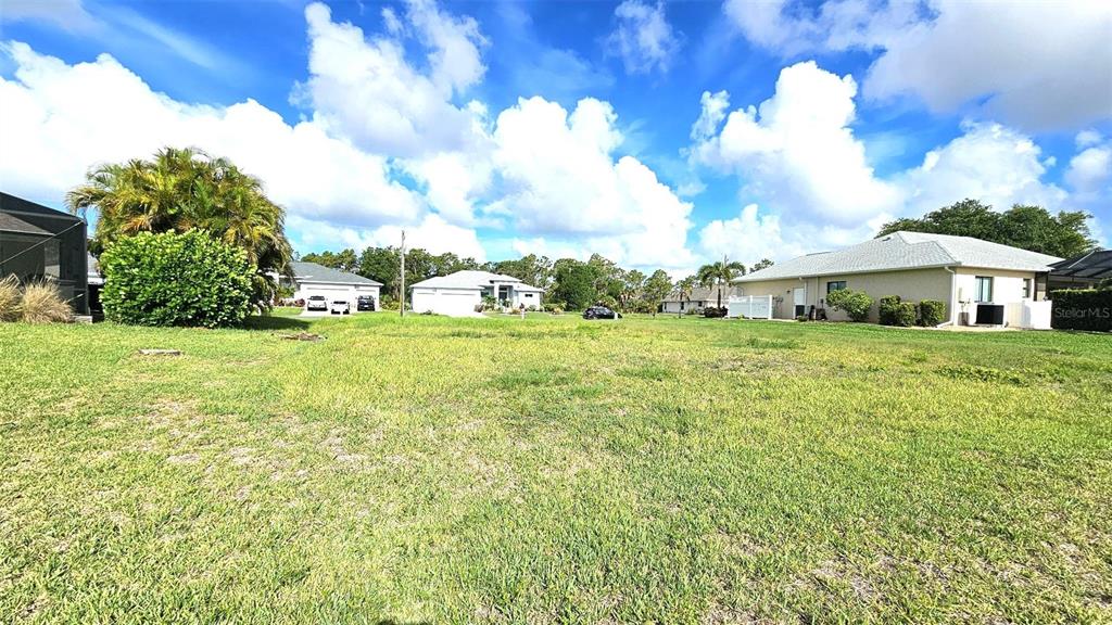 A large, grassy vacant lot is situated in a residential neighborhood under a cloudy sky — 144 LONG MEADOW LANE, ROTONDA WEST, FL