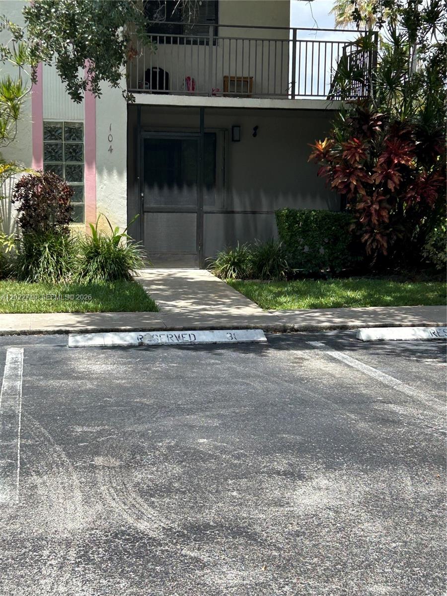 A ground-level apartment entrance features a screen door, a small walkway, and a reserved parking space — 413 Lakeview Dr # 104, Weston FL 33326, WESTON, FL