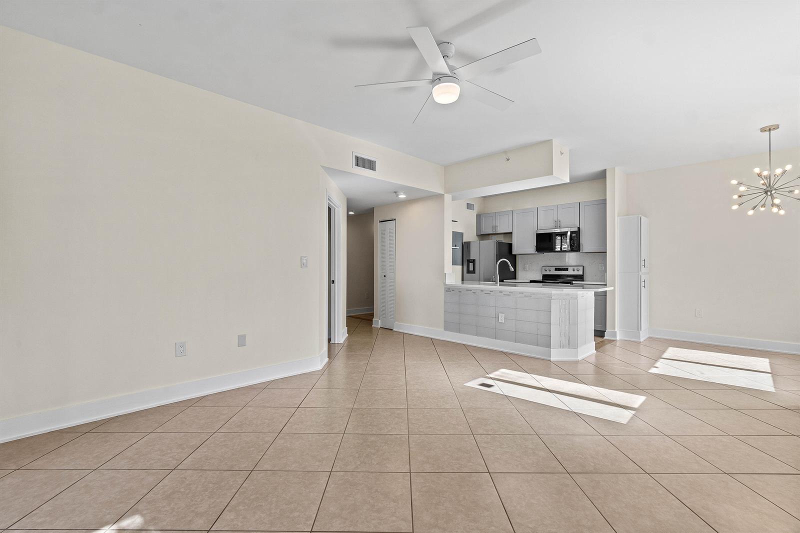 An open-concept living area features a tiled floor, a kitchen with gray cabinets, and a ceiling fan — 1000 Scotia Drive # 102, Hypoluxo FL 33462, HYPOLUXO, FL