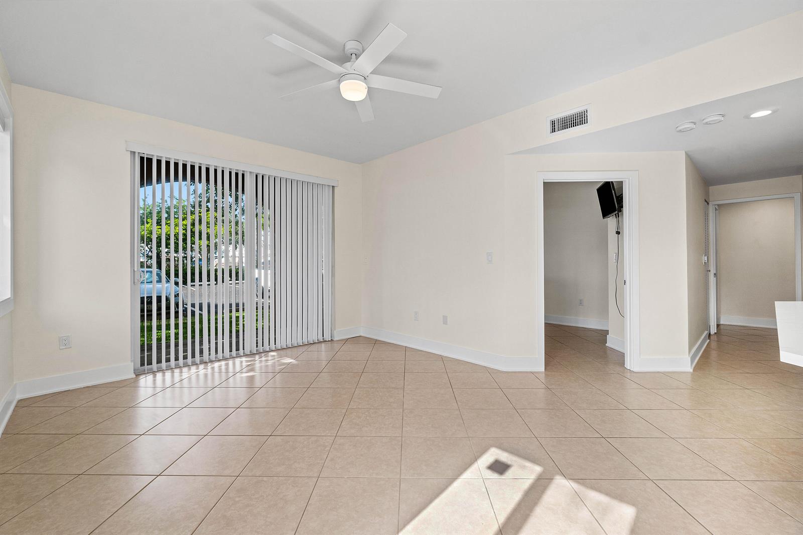 An empty room features beige tile flooring, a ceiling fan, and sliding glass patio doors — 1000 Scotia Drive # 102, Hypoluxo FL 33462, HYPOLUXO, FL