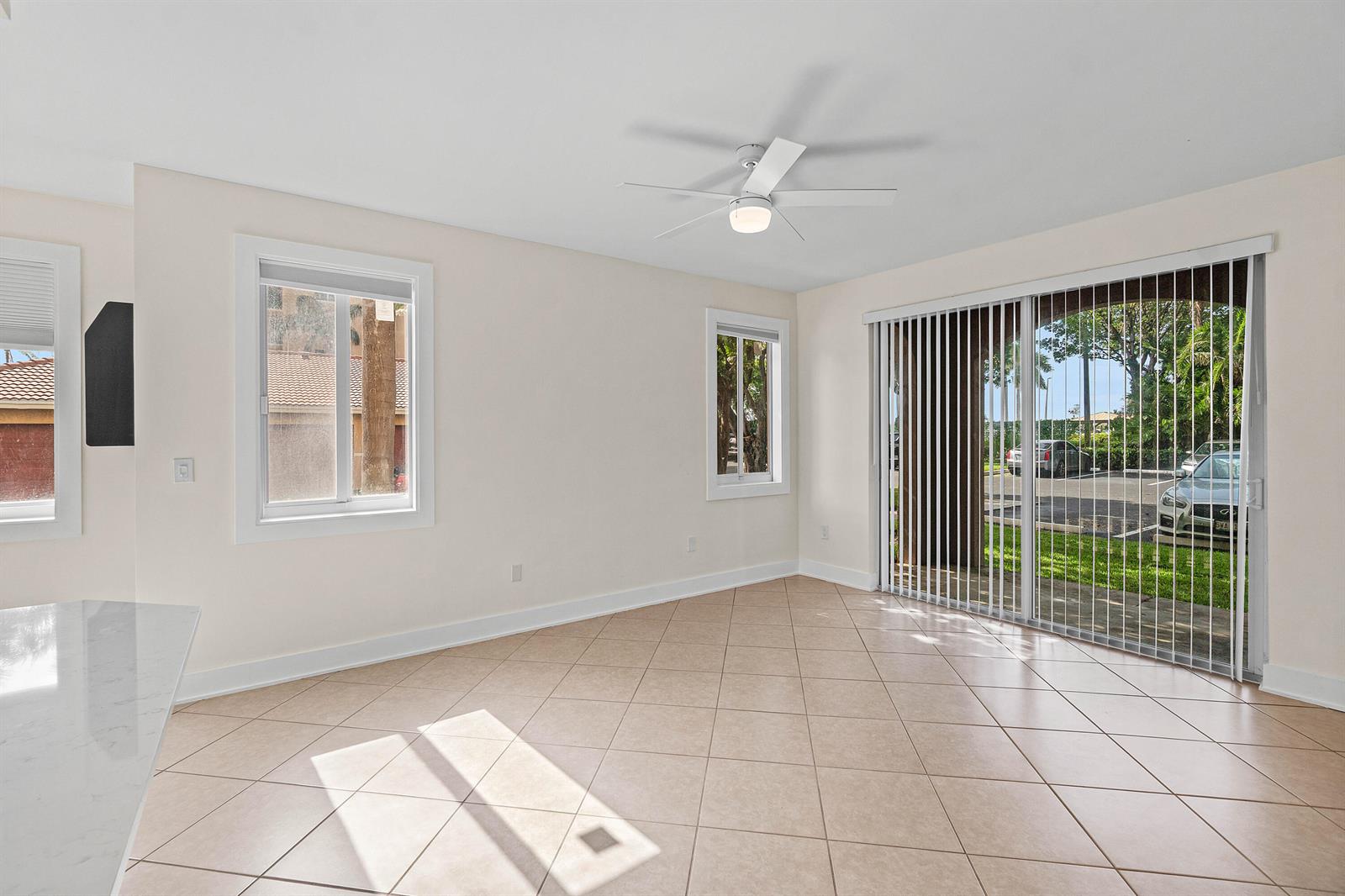 An empty room features beige tile flooring, white walls, a ceiling fan, and sliding glass doors — 1000 Scotia Drive # 102, Hypoluxo FL 33462, HYPOLUXO, FL