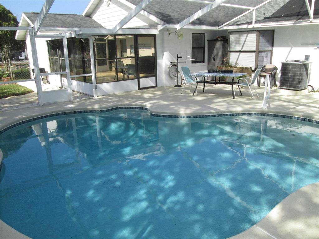 A swimming pool sits on a concrete patio enclosed by a screened-in lanai — 155 VILLAGE LANE, DAYTONA BEACH, FL