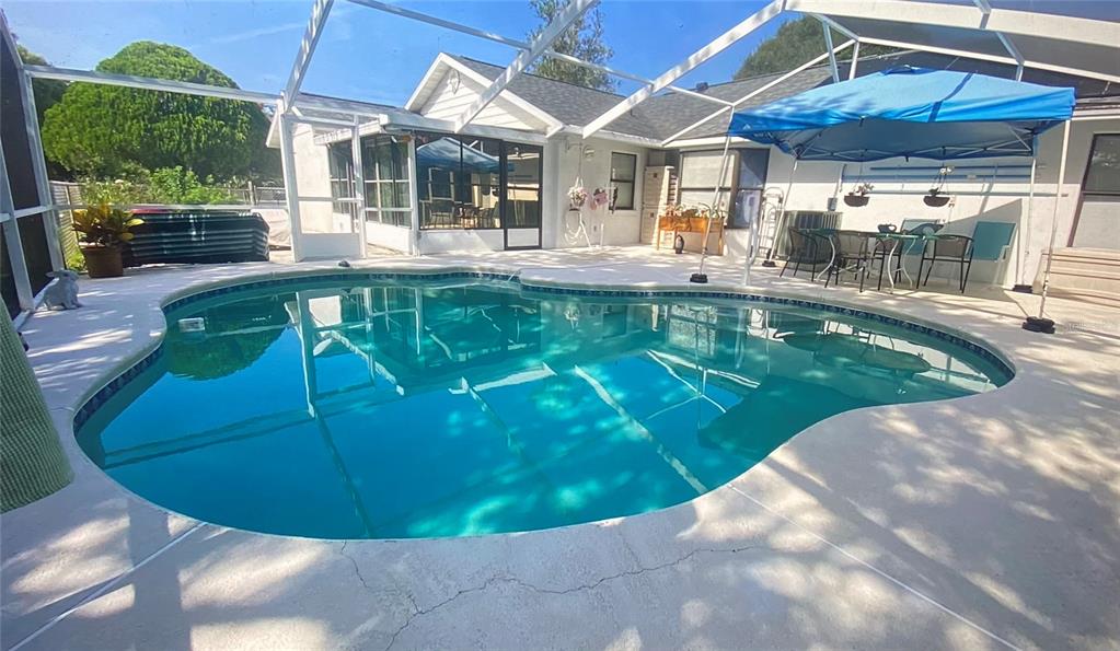 A swimming pool sits on a concrete patio enclosed by a screened lanai — 155 VILLAGE LANE, DAYTONA BEACH, FL