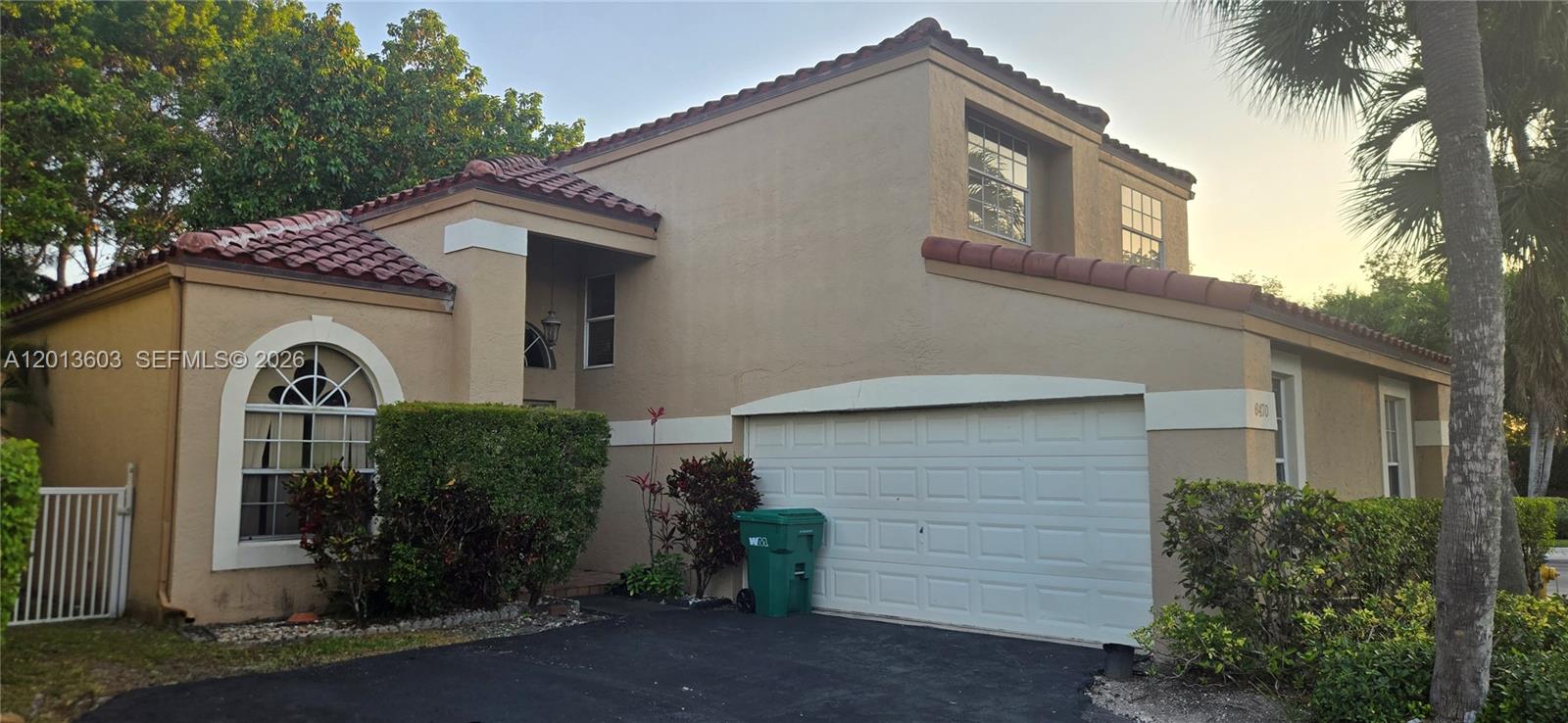 A two-story stucco house features a tile roof, a white garage door, and landscaping — 6470 NW 77th Pl, Parkland FL 33067, PARKLAND, FL