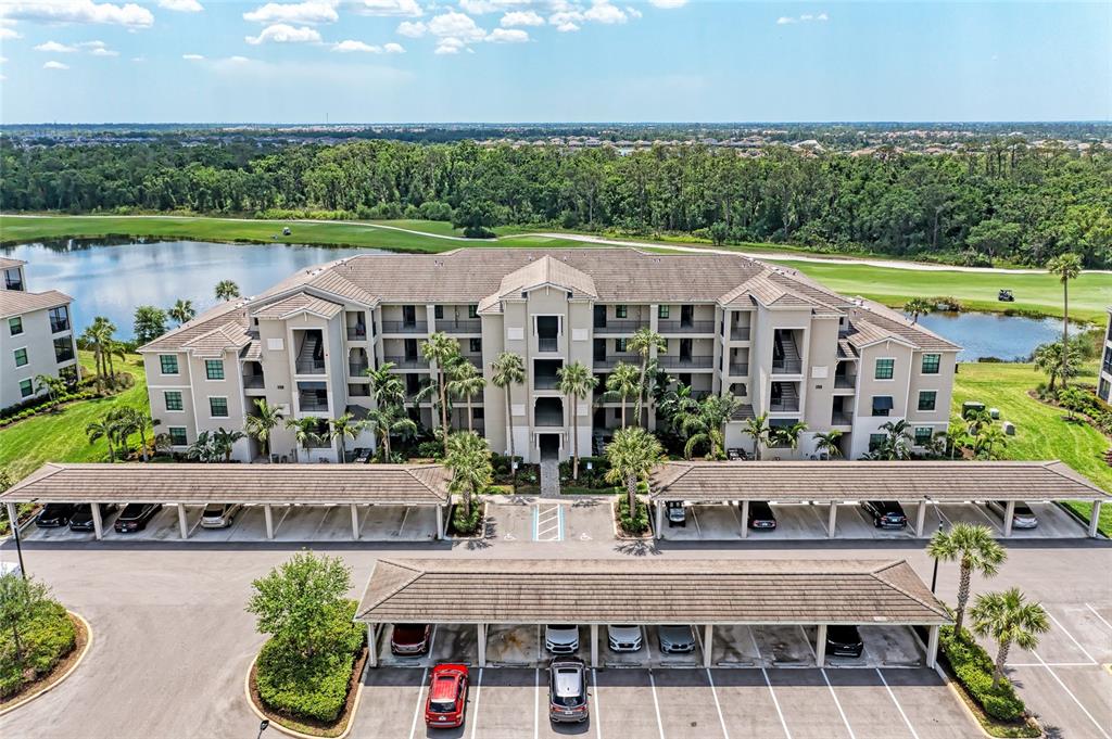 An aerial view shows a multi-story apartment building with covered parking structures and surrounding ponds — 17520 GAWTHROP DRIVE UNIT 304, BRADENTON, FL