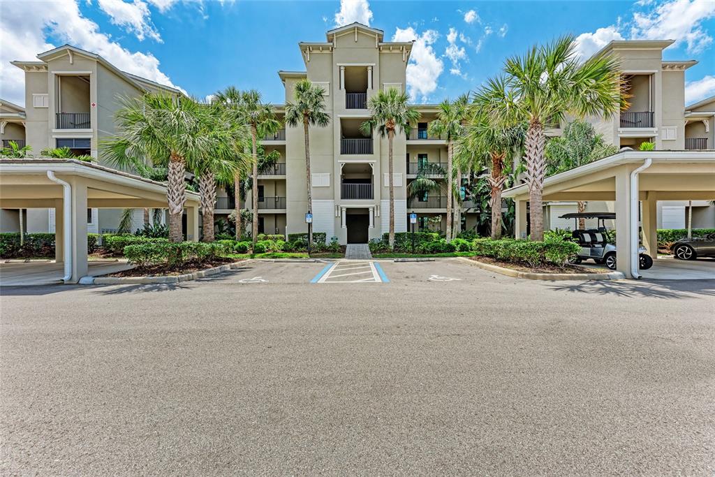A multi-story apartment building exterior features covered parking spaces and palm trees in front — 17520 GAWTHROP DRIVE UNIT 304, BRADENTON, FL