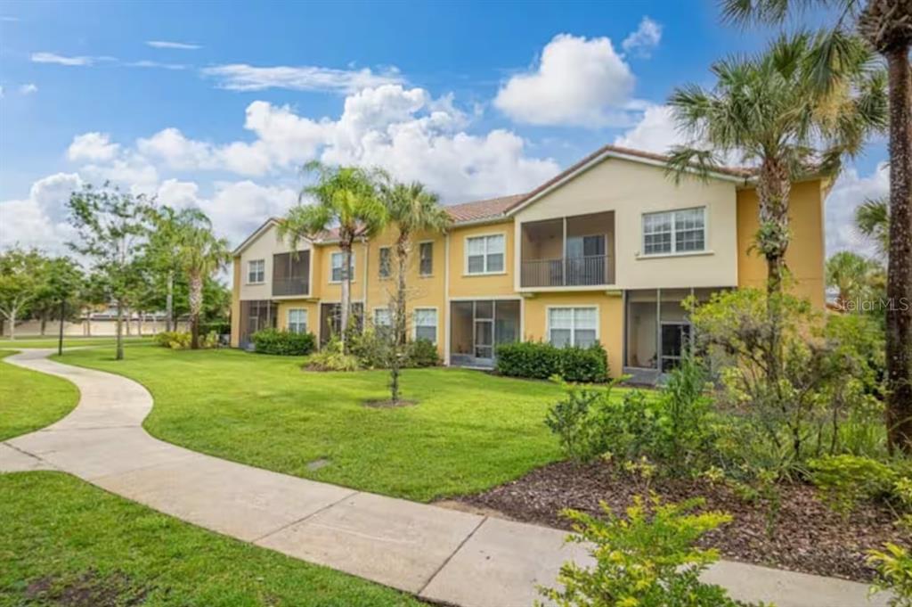 A two-story apartment building with tan stucco walls, screened balconies, and a paved walkway — 2888 OAKWATER DRIVE UNIT 2888, KISSIMMEE, FL