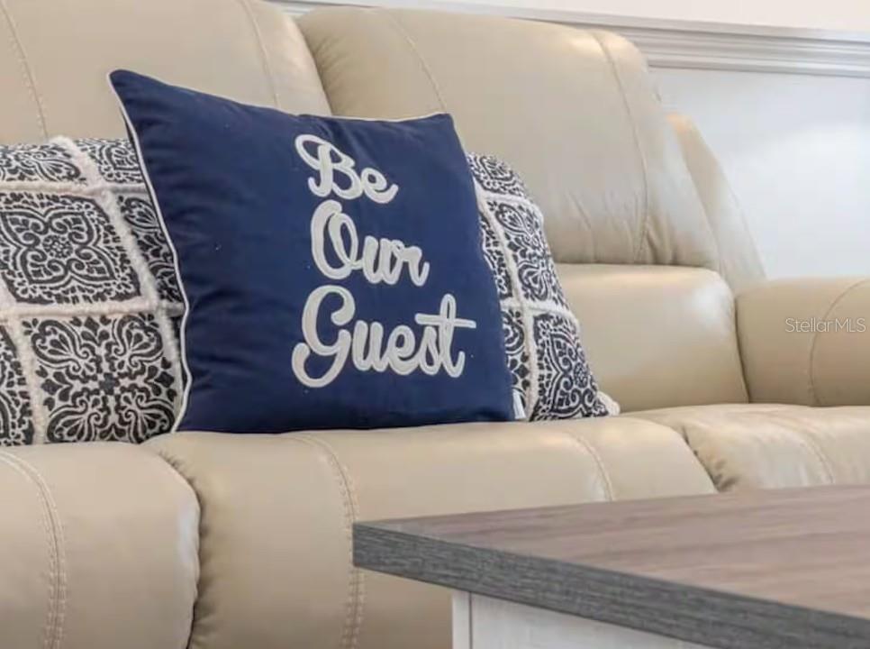A blue decorative pillow with white text sits on a light-colored leather sofa — 2888 OAKWATER DRIVE UNIT 2888, KISSIMMEE, FL