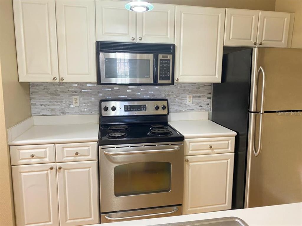 A kitchen features white cabinets, stainless steel appliances, and a tiled backsplash — 14341 FREDRICKSBURG DR DRIVE UNIT 1007, ORLANDO, FL