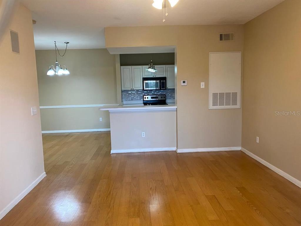 A view of a living area with hardwood floors looking toward a kitchen with white cabinets — 14341 FREDRICKSBURG DR DRIVE UNIT 1007, ORLANDO, FL