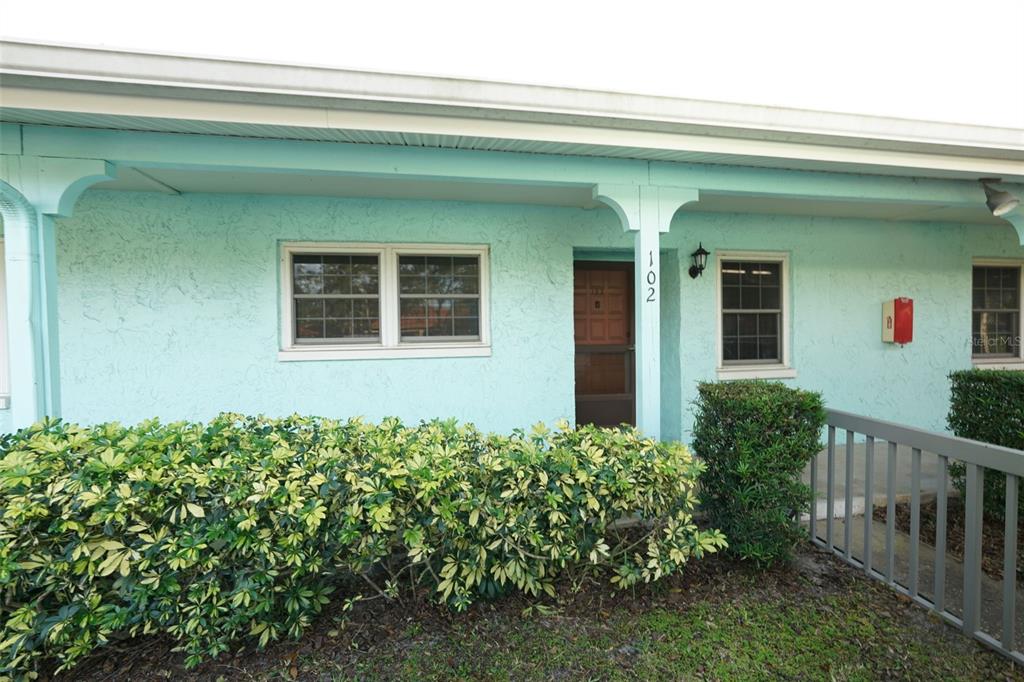 A light blue building exterior features a front door labeled 102 and landscaping — 2465 NORTHSIDE DRIVE UNIT 102, CLEARWATER, FL
