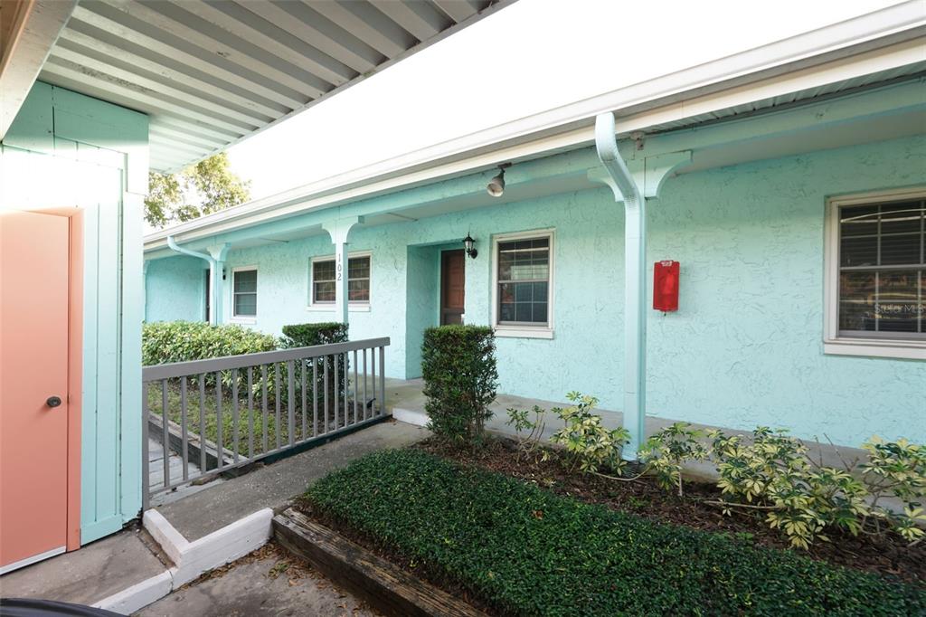 A light blue exterior wall features a front door, two windows, and a green shrub — 2465 NORTHSIDE DRIVE UNIT 102, CLEARWATER, FL