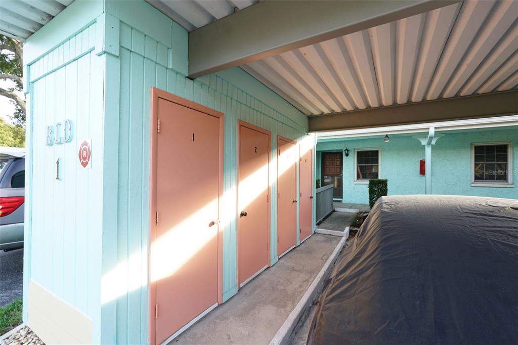 A covered walkway features a row of numbered storage doors against a light blue building — 2465 NORTHSIDE DRIVE UNIT 102, CLEARWATER, FL