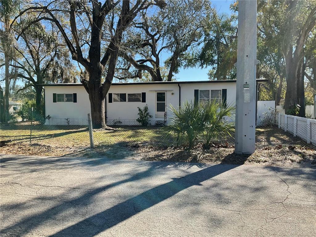 A single-story mobile home with white siding stands behind a chain-link fence and trees — 4707 E YUKON STREET, TAMPA, FL