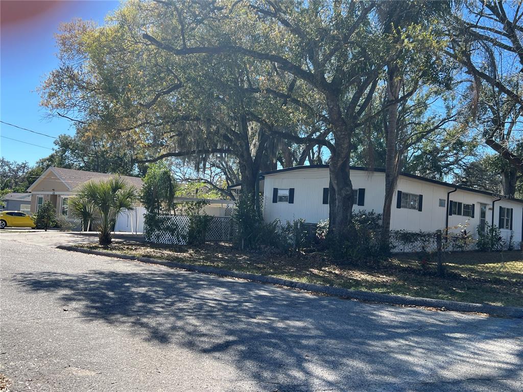 A white mobile home sits on a street corner under large, mature oak trees — 4707 E YUKON STREET, TAMPA, FL