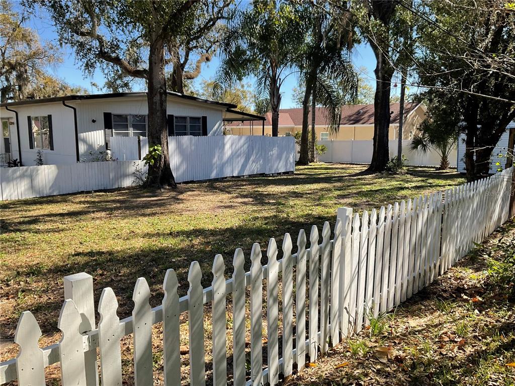 A white picket fence encloses a grassy yard with trees and a nearby house — 4707 E YUKON STREET, TAMPA, FL
