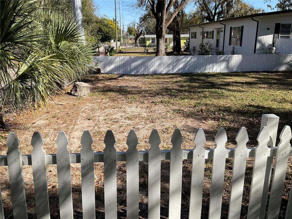 A fenced-in backyard with sandy soil, sparse grass, and a tree stump — 4707 E YUKON STREET, TAMPA, FL