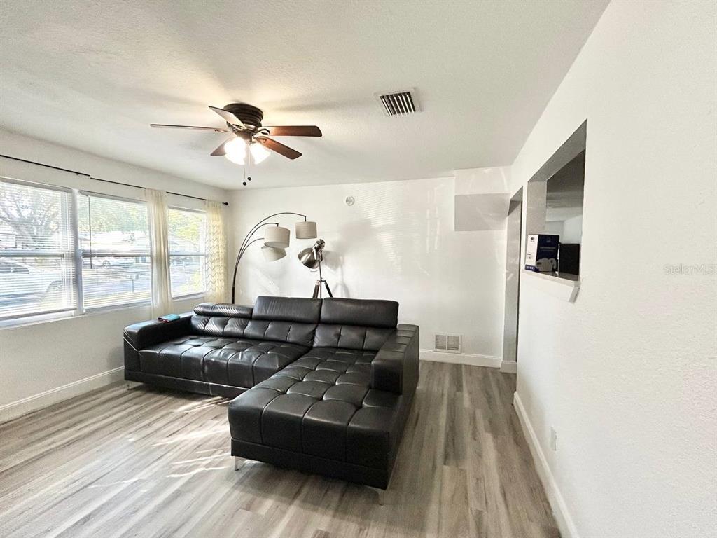 A living area with light wood-look flooring features a kitchen pass-through window and ceiling fan — 1280 BERTLAND WAY, CLEARWATER, FL
