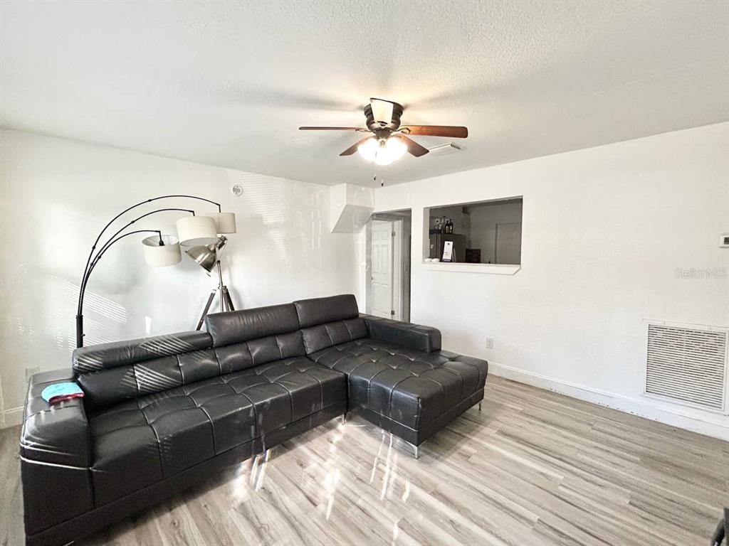 A kitchen features white cabinets, stainless steel appliances, a tiled backsplash, and light wood flooring — 1280 BERTLAND WAY, CLEARWATER, FL
