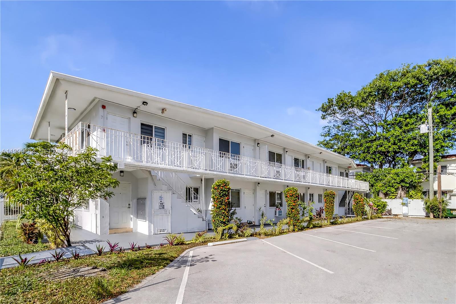 A two-story white apartment building features an exterior balcony, stairs, and a paved parking lot — 8129 Abbott Ave # 10, Miami Beach FL 33141, MIAMI BEACH, FL