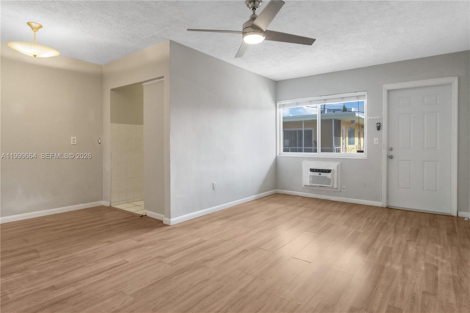 This room features light wood-look flooring, a ceiling fan, a window air conditioner, and a door — 8129 Abbott Ave # 10, Miami Beach FL 33141, MIAMI BEACH, FL