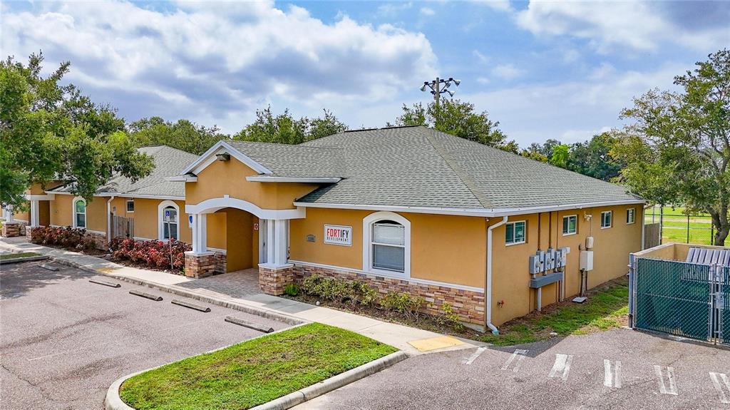A single-story commercial building with tan stucco walls, stone accents, and a green shingled roof — 7318 W COMANCHE AVENUE, TAMPA, FL