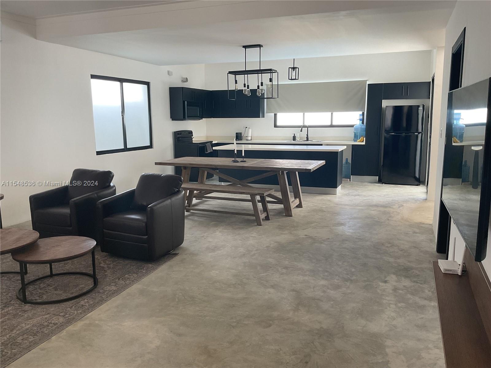 An open-concept kitchen and living area features dark cabinetry, a wooden dining table, and concrete floors — 3 SW Calle el sol, Re, Re