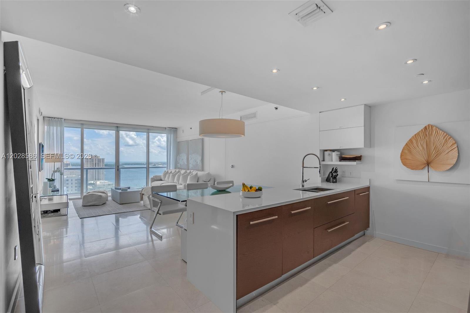 A modern kitchen with wood cabinets and a white island overlooks a living area — 465 Brickell Ave # 2703, Miami FL 33131, MIAMI, FL