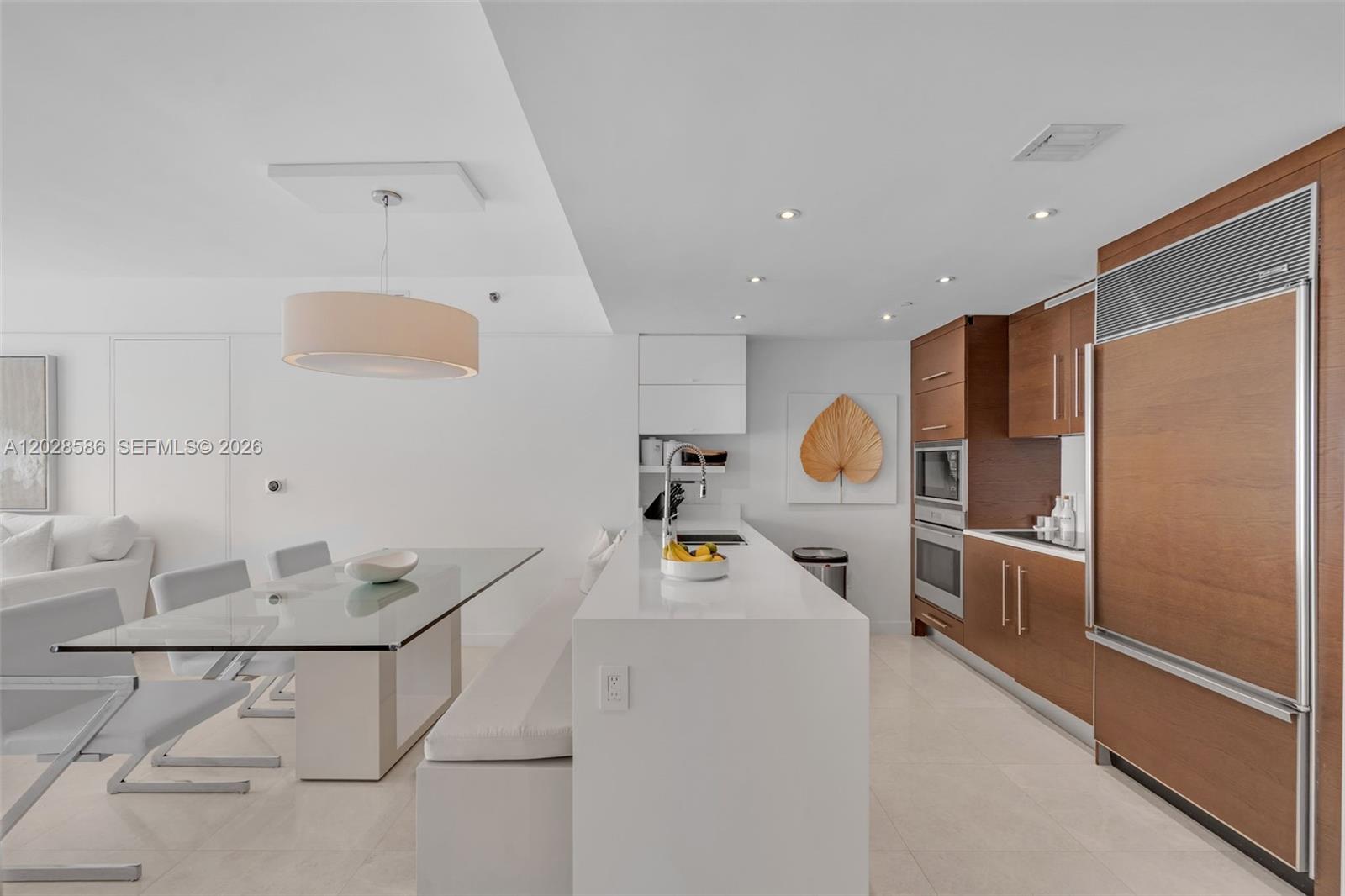 A modern kitchen features white countertops, wood cabinetry, and an adjacent glass dining table — 465 Brickell Ave # 2703, Miami FL 33131, MIAMI, FL