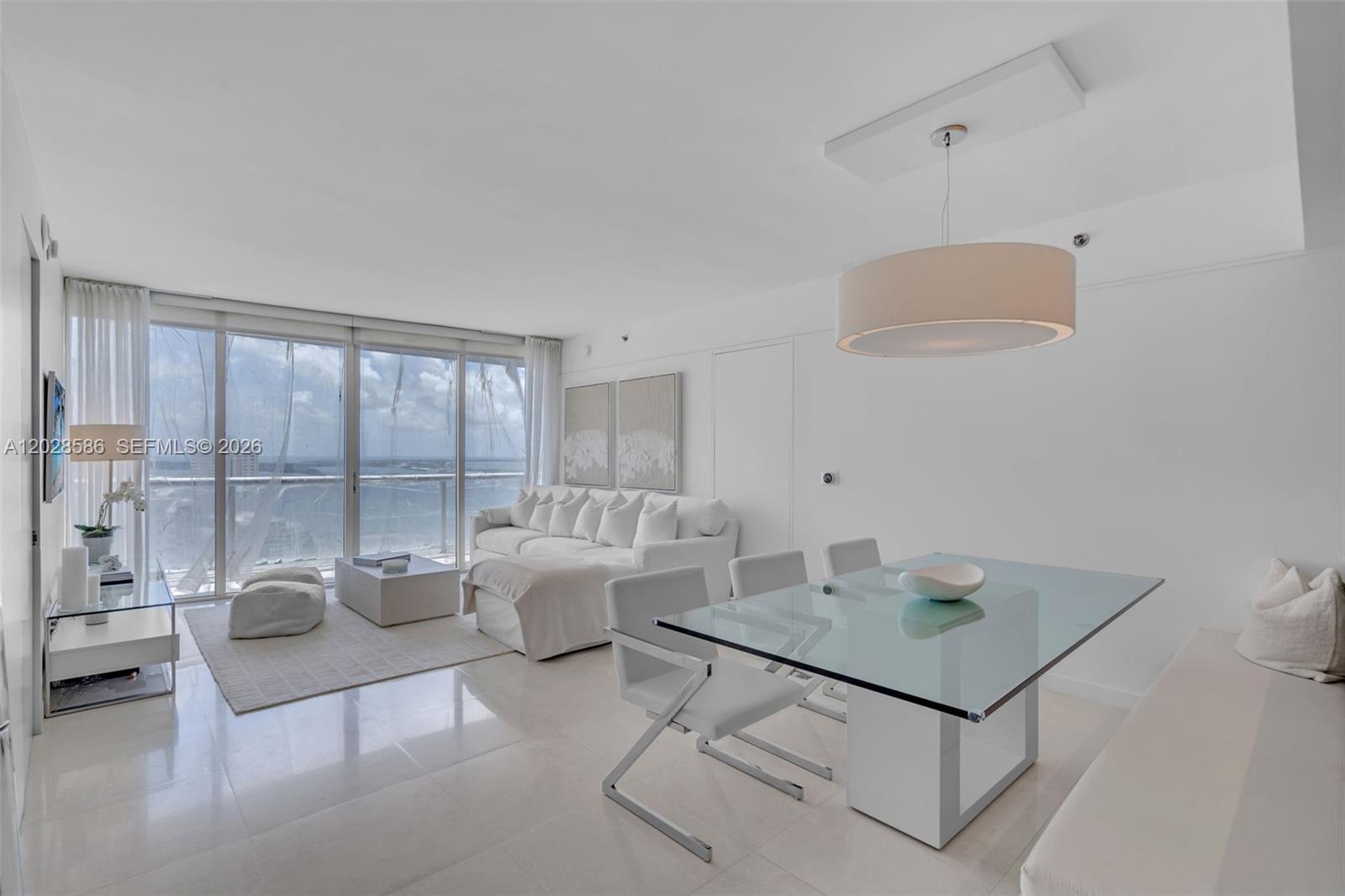 A bright, modern living and dining area features white furniture, glass tables, and floor-to-ceiling windows — 465 Brickell Ave # 2703, Miami FL 33131, MIAMI, FL