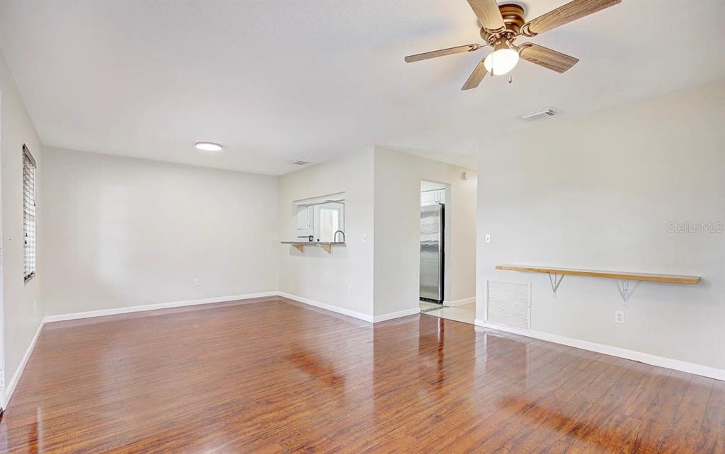 An empty living room features hardwood floors, a ceiling fan, and a kitchen pass-through window — 6319 S CHURCH AVENUE, TAMPA, FL